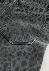Grauer Denimstoff mit einem subtilen Leopardenmuster. Eine Gesäßtasche mit einer ausgeprägten Form und sichtbaren Nähdetails.