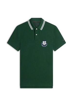Dunkelgrünes Poloshirt mit weißen Doppellinien am Kragen, zwei Knöpfen und einem blauen und weißen Tommy Hilfiger Wappen auf der Brust.
