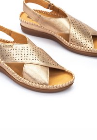 Sandales en cuir doré avec des brides croisées perforées, une semelle intérieure rembourrée et un bord tressé sur la semelle en caoutchouc pour un détail supplémentaire.