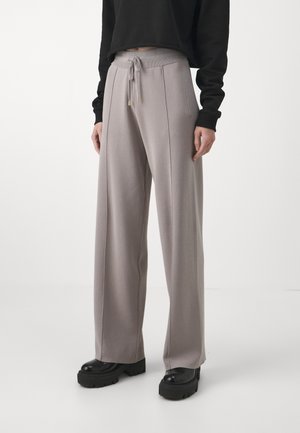 Pantalones de pierna ancha color gris claro con cintura de cordón, detalles dorados y bolsillos laterales, combinados con zapatos de plataforma negros.