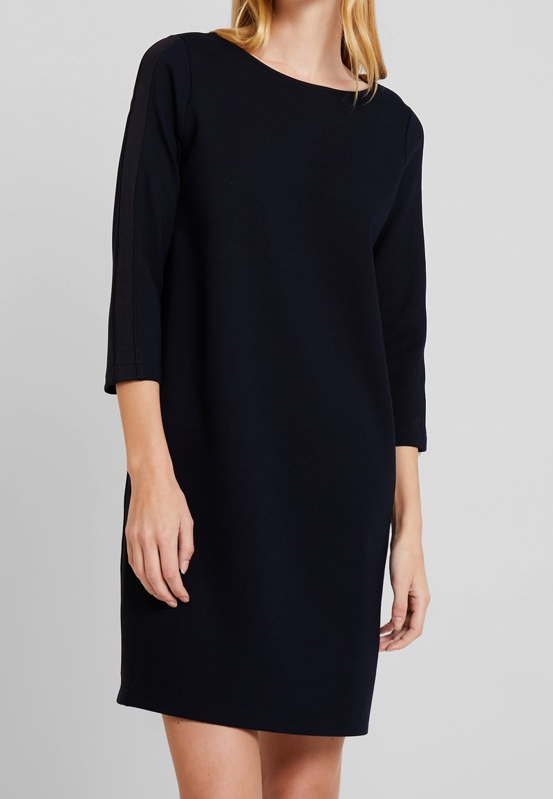 Robe bleu marine, longueur genou, en tissu lisse et doux avec manches trois-quarts et encolure ronde. Design minimaliste, sans motifs ni accents.