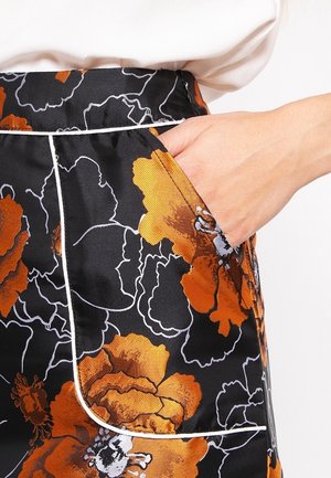 Pantalon en satin à motif floral avec des fleurs orange et noires, doté d'une poche latérale et d'un passepoil blanc contrastant le long de la taille et des bords de la poche.