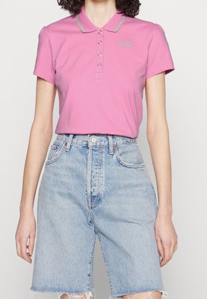 Lyserød polo med sølvdetaljer, tre-knaps lukning og korte ærmer. Kombineret med lyseblå denimshorts med frynser.