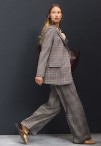 Gray plaid suit with wide-leg trousers and a tailored blazer, paired with brown sandals and a dark tote bag.