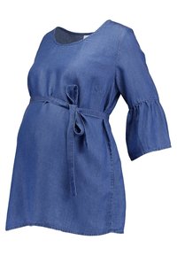 Denim graviditetstopp med avslappnad passform, fjärilskjolar och ett knytbälte vid midjan. Har rundad halsringning och ljusare sömnadsdetaljer.