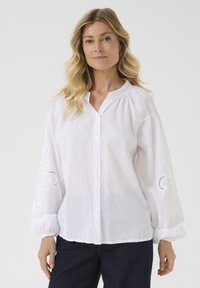 White button-up shirt with embroidered patterns on the sleeves, soft linen texture, relaxed fit, and slightly gathered neckline.