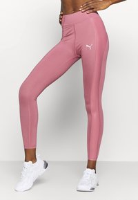 Leggings de talle alto en color rosa, fabricados con un material elástico, que presentan una textura suave y el logo blanco de Puma en el muslo izquierdo.
