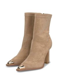 Botas de ante beige hasta el tobillo con un tacón grueso, punta afilada y acentos metálicos dorados en la puntera. La parte superior presenta detalles de costura limpios.