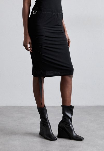 Schwarzer Bleistiftrock mit einem elastischen Bund und silbernen Hardware-Akzenten. Kombiniert mit schwarzen Keilbooties, die ein elegantes Design haben.