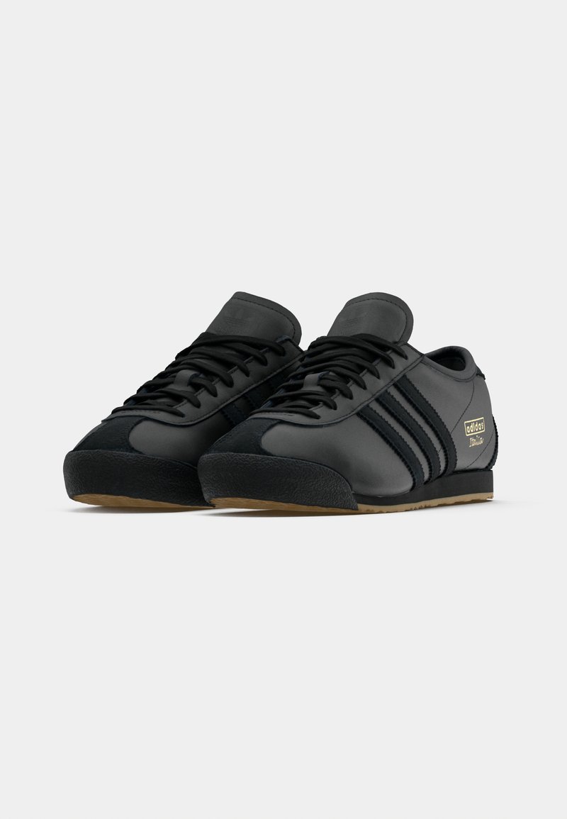 Black athletic shoes with a smooth leather upper, suede accents, three stripes, and a textured rubber sole. Gold logo detail on side.