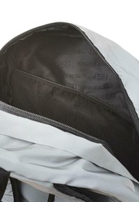 Interior de mochila gris con una textura suave. Cuenta con un bolsillo de malla negra y un sutil patrón de rayas en el forro. Cierre de cremallera.