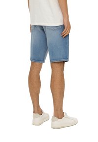 Jasnoniebieskie szorty dżinsowe o luźnym kroju, z podwiniętym dołem i dwoma tylnymi kieszeniami, zestawione z białymi sneakersami.