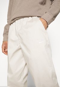 Nike ljusbeige sweatpants med elastisk midjeresår, sidofickor och broderad logotyp i vitt. Materialet verkar mjukt och lätt.