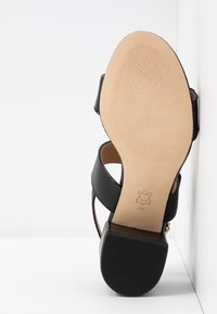 Sandale en cuir noir avec semelle beige et talon bloc, vue par en dessous, taille 7M, avec marquage du matériau cuir sur la semelle.