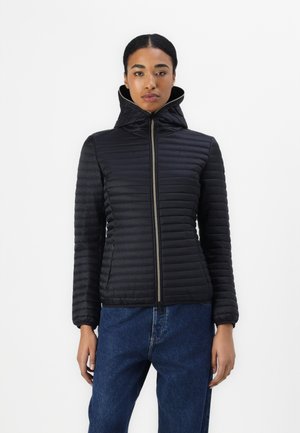 Giacca nera trapuntata con colletto alto e cappuccio, dotata di zip frontale e polsini elasticizzati. Abbinata a jeans in denim blu.