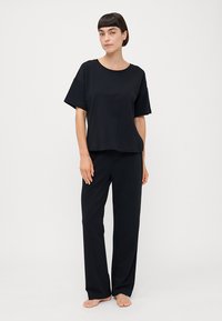 Svart lounge-sett som inkluderer en kortermet topp med rund hals og rett-ben bukser, laget av mykt stoff med minimalistisk design.