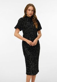 Melnā aplikāciju kleita ar augstu apkakli un īsām piedurknēm, pieguļoša silueta, līdz ceļiem, spīdīga tekstūra un smalkas aplikāciju detaļas.