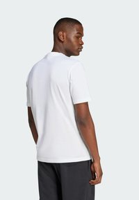 Witte katoenen t-shirt met korte mouwen, ronde halslijn en een relaxte pasvorm, gedragen door een model dat iets scheef naar voren kijkt tegen een lichte achtergrond.