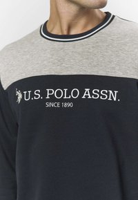 Tengerészkék és szürke, hosszú ujjú pamut pulóver, mandzsettás nyakkivágással, hímzett logóval és kontrasztos színblokkokkal.
