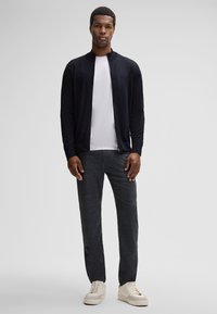 Czarny kardigan, biały t-shirt, szare spodnie o fakturze oraz białe trampki. Kardigan ma bezkołnierzowy krój, oferujący nowoczesną sylwetkę.