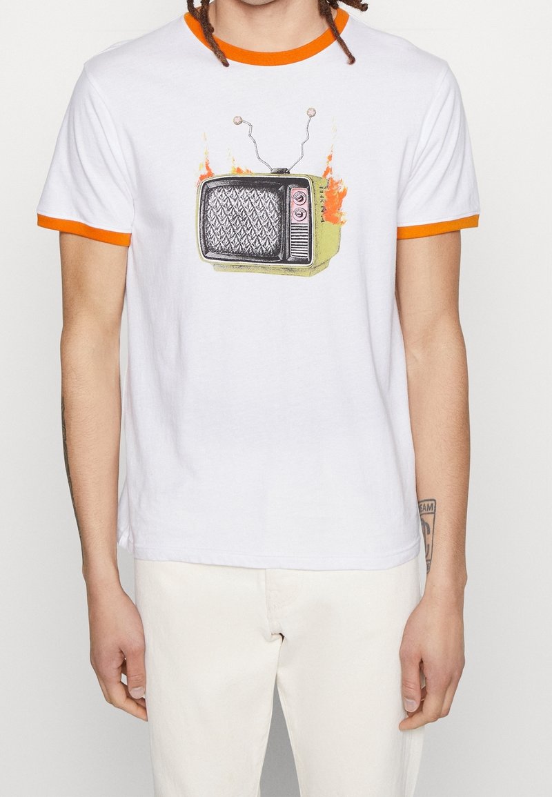 Person iført en hvid t-shirt med orange krave og ærmekant, der har et retro fjernsyn i brand grafik i midten af brystet.