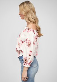 Blusa s cvijetnim uzorkom s otvorenim ramenima od bijelog materijala, s uzorcima ružičastih cvjetova i leptira, s napučenim rukavima i elastičnim rubovima.