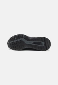 Semelle de chaussure de sport noire avec un caoutchouc texturé, présentant des motifs de traction multidirectionnels et un détail de semelle intermédiaire bien en évidence portant l'inscription "TRAXION".