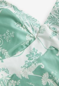 Šviesiai žalios ir baltos spalvų gėlėmis marginta medžiaga, minkšta tekstūra, su išsiskiriančiais lapais ir gėlėmis, su prigludusia iškirpės detalė.