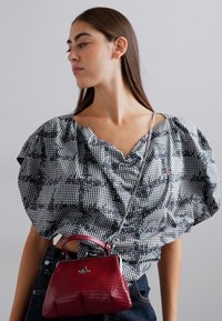 Blusa de padrão gingham em preto e branco com mangas volumosas, acompanhada de uma pequena bolsa texturizada vermelha com um fecho prateado.