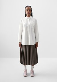 Cămașă albă cu mâneci lungi, asortată cu o fustă maro plisată. Purtați cu adidași roz și șosete albe. Design simplu și croi lejer.