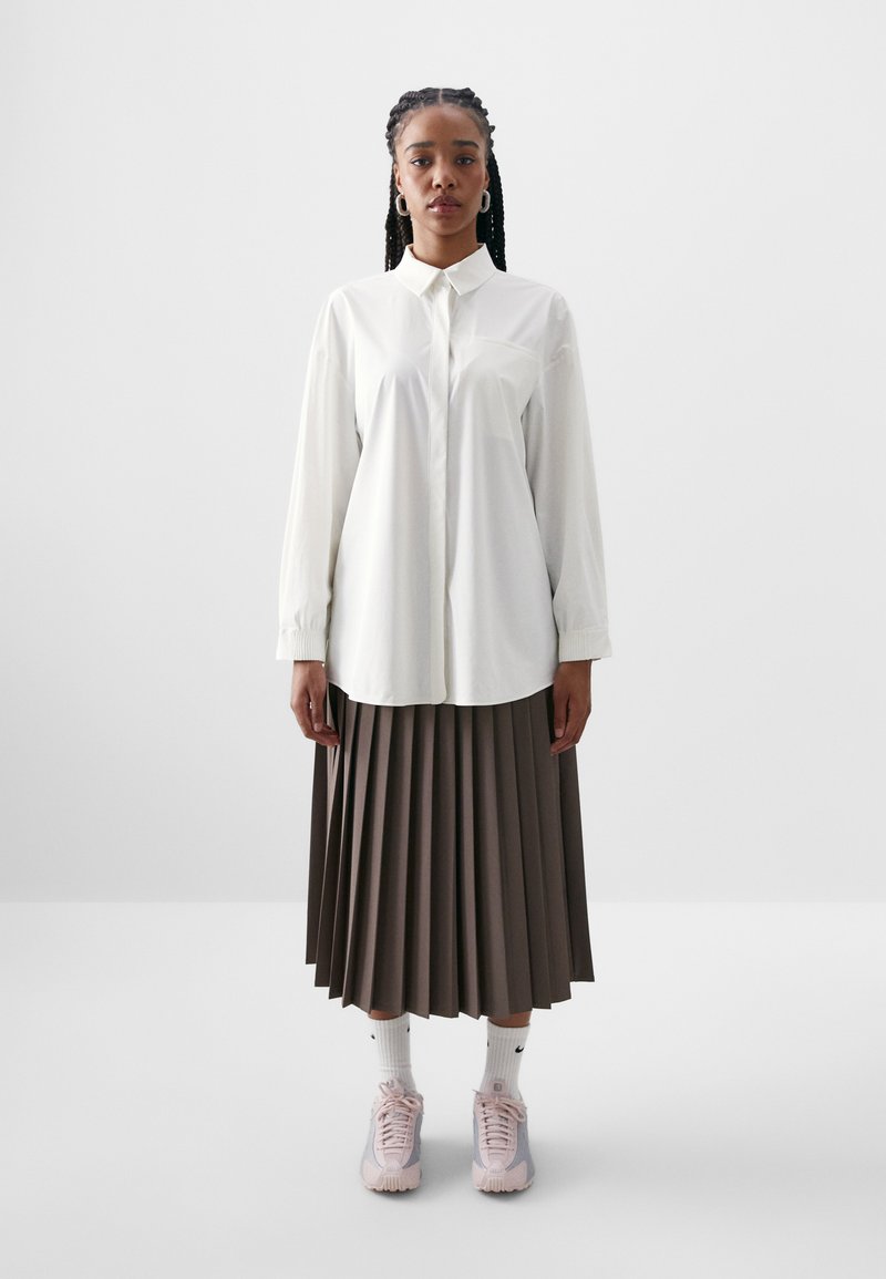 Cămașă albă cu mâneci lungi, asortată cu o fustă maro plisată. Purtați cu adidași roz și șosete albe. Design simplu și croi lejer.