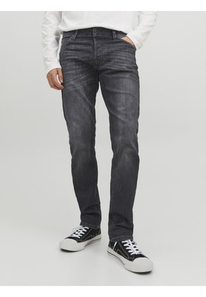 Dunkelgraue Jeans mit schlankem Schnitt, aus Denim. Verfügt über fünf Taschen, subtile Verblassung und einen klassischen Knopf- und Reißverschluss. Kombiniert mit schwarzen Sneakers.