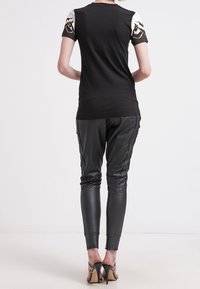 Černý top s krátkým rukávem, zdobený bílými a zlatými akcenty na ramenou, spárovaný s úzkými černými koženými kalhotami a podpatky.