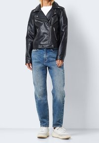 Czarna skórzana kurtka motocyklowa ze srebrnymi zamkami i guzikami, w połączeniu z wyblakłymi niebieskimi dżinsami i białymi trampkami. Luźny, codzienny zestaw.