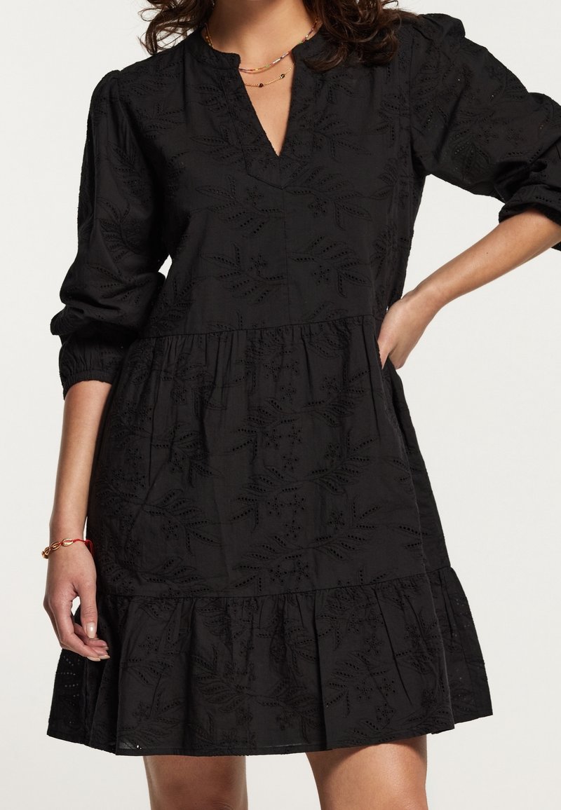 Robe en coton noire avec manches longues, encolure en V et ourlet à volants. Présente des motifs de feuilles brodés et des poignets de manches élastiqués.