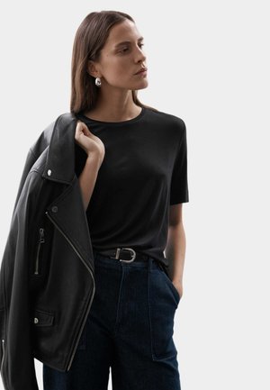 Czarna koszulka z krótkim rękawem w połączeniu z czarną skórzaną kurtką, niebieskimi spodniami typu high-waist i srebrną klamrą, prezentująca minimalistyczny styl.