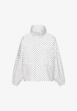 Fehér, könnyű súlyú dzseki fekete pöttyökkel, magas gallérral, rugalmas mandzsettákkal és elülső zsebekkel, egyszerű háttéren.