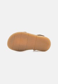 Brun sandal med en struktureret gummisål, der har vandrette riller og en lille hæl. Fodsålen er polstret for komfort.