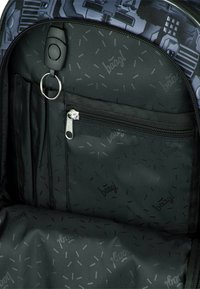 Interno di uno zaino nero con diversi scomparti per la memorizzazione, inclusa una tasca con zip, e un motivo sottile che presenta il nome del marchio.
