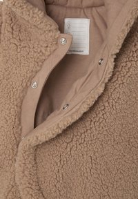 Beige fleece jacket with a textured, fluffy exterior and smooth inner lining. Features snap buttons and a care label for size and instructions.