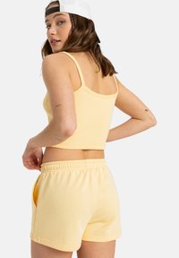 Lichtgeel geribbeld crop top met dunne bandjes, gedragen met bijpassende zachte shorts met zijzakken en een elastische tailleband.