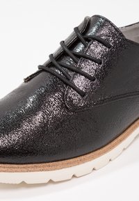 Chaussure à lacets en cuir noir texturé avec semelle intermédiaire beige et semelle extérieure en caoutchouc blanc robuste, présentée en gros plan.