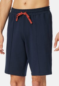 Marineblauwe shorts met een elastische tailleband, voorzien van een rode trekkoord. Gemaakt van een zachte stof, met zijzakken en een relaxte pasvorm.