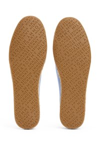 Semelles de sneakers avec une surface en caoutchouc brun texturé affichant le nom de la marque en relief. Les panneaux latéraux sont d'un bleu clair avec une finition lisse.