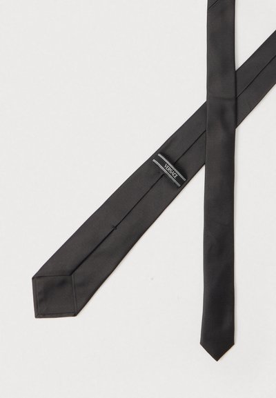 Juodas šilkinis kaklaraištis su lygia, blizgia tekstūra, turintis aštrų galą ir siuvinėtą Versace etiketę vienoje pusėje.