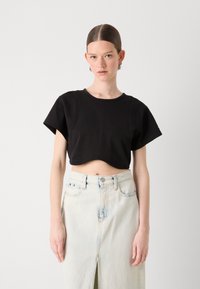 Fekete, rövid ujjú, cropped póló, puha tapintással és ívelt alsó résszel, amelyet egy világos mosott farmer szoknyával viselnek, elől hasítékkal.