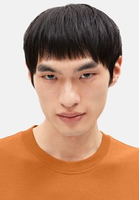 Oranger Rundhals-Sweatshirt mit geripptem Ausschnitt, getragen von einem Model mit kurzem schwarzen Haar und neutralem Gesichtsausdruck.