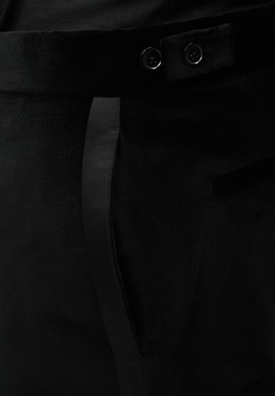 Κοντινό πλάνο μαύρου παντελονιού από ύφασμα που δείχνει τη μέση με δύο κουμπιά και μια κατακόρυφη πλαϊνή τσέπη.