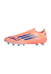 Botín de fútbol de color coral brillante con rayas y tacos azules, diseño esbelto, ligero, sin cordones visibles.