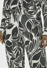 Zwart-wit bloemenpatroon outfit met een knoopsluiting bovenstuk en broek met elastische tailleband, met een gestructureerde stof en een vloeiende ontwerp.